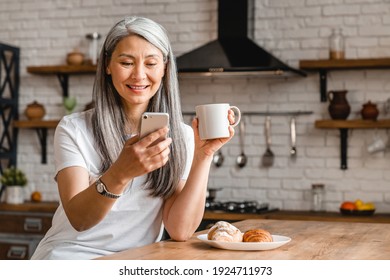 Happy middle-aged woman using smart phone during the breakfast in the kitchen - Powered by Shutterstock