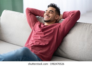 Happy Middle-eastern Guy In Casual Chilling At Home, Reclining On Couch With Closed Eyes And Smiling. Relaxed Young Arab Man Enjoying His New Comfortable Couch, Leaning Back, Copy Space