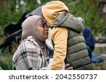 Happy middle-eastern mother in headscarf touching foreheads with daughter while finding her after escape from battlefield