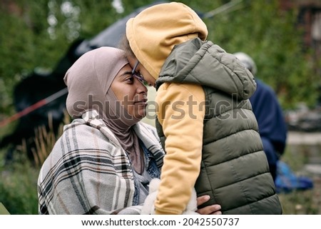 Happy middle-eastern mother in headscarf touching foreheads with daughter while finding her after escape from battlefield