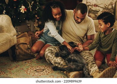 Happy military family playing with their cat at Christmas. Military dad reuniting with his children at home. Soldier spending quality time with his family after military deployment.