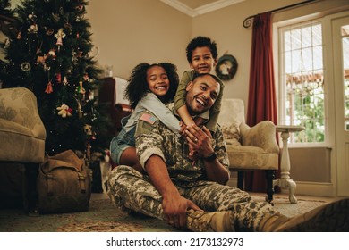 Happy military family smiling joyfully while spending Christmas together. Cheerful military dad reuniting with his children at Christmas. Soldier spending quality time with his family after deployment - Powered by Shutterstock