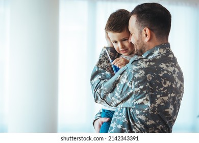 Happy Military Man With His Son At Home. An Emotional Military Father, Dressed In Camouflage, Holds His Young Son In Arms In Greeting After Returning Home From A Tour Of Duty Overseas.