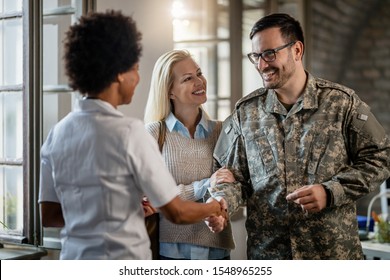 Happy military man shaking hands with female doctor while being with his wife at medical counselling.