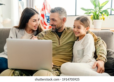 Happy Military Man Smiling And Hugging His Family While Using Laptop Indoors