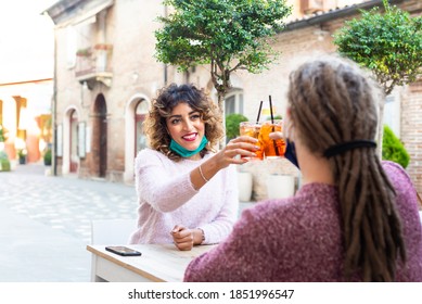 Happy Millenial Couple Wearing Protective Face Mask Having Fun Together At Bar Cafeteria. New Normal Lifestyle Concept With Young People On Positive Mood Drinking Cocktails On A Open Air Restaurant