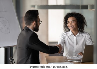 Happy millennial african American businesswoman shake hand greeting or get acquainted with male colleague, smiling biracial woman employee handshake man partner, closing deal at negotiations