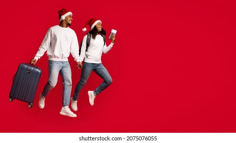 Happy Millennial African American Couple With Backpacks, Luggage And Passport With Tickets Running Towards Copy Space On Red Studio Background, Travelling While Winter Holidays, Panorama