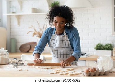 Happy millennial African American woman in apron cooking bakery food in home kitchen, rolling dough, smiling. Blogger, baker, chef enjoying job, making cookies, preparing pastry dessert, biscuit, cake - Powered by Shutterstock