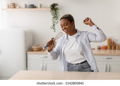 Happy Millennial African American Woman With Closed Eyes Singing At Imaginary Microphone At Kitchen Interior. Housewife Superstar Enjoys Free Time, Food Blogger At Home During Covid-19 Quarantine