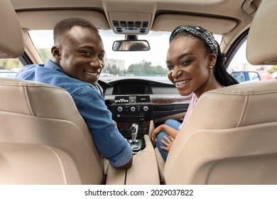 Happy Millennial Afro American Couple Posing In Their New Auto, Looking At Backseat, Cheerfully Smiling At Camera While Making Test Drive. Cheerful Black Man And Woman Going Summer Vacation By Car