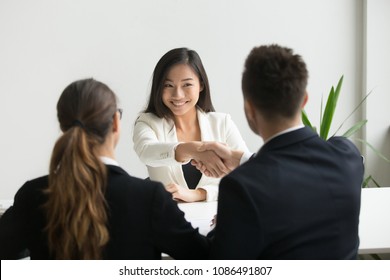 Happy millennial asian applicant getting hired shaking hand of hr, employer handshaking successful smiling chinese candidate congratulating with job interview win offering employment contract concept