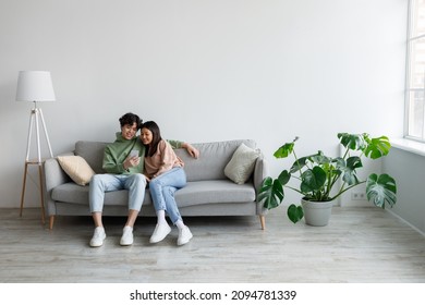 Happy Millennial Asian Couple Using Cellphone, Texting And Browsing Internet, Relaxing On Couch Indoors, Copy Space. Relaxed Young Family Using Mobile Application, Resting At Home