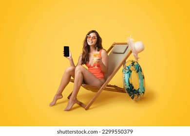 Happy millennial asian lady in swimsuit, sunglasses with inflatable ring sit on deck chair, enjoy tropical cocktail, rest, show smartphone with blank screen isolated on orange studio background - Powered by Shutterstock