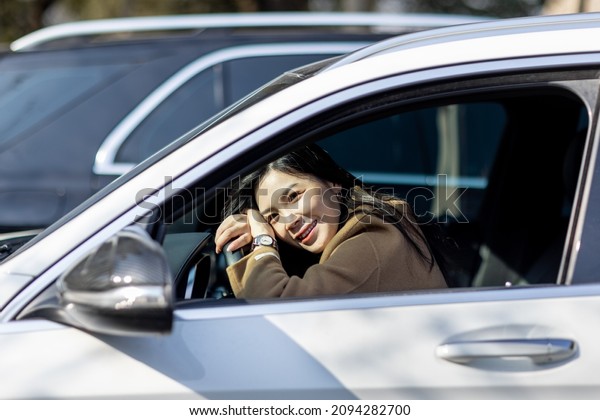 Happy millennial asian woman holding steering\
wheel when driving car at sunny autumnal day with glad positive\
emotion, being satisfied with unforgettable journey by car, sitting\
on seat, enjoying