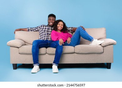 Happy millennial black couple relaxing on sofa, smiling at camera on blue studio background, full length. Young boyfriend and girlfriend resting on couch, having break together on free time - Powered by Shutterstock