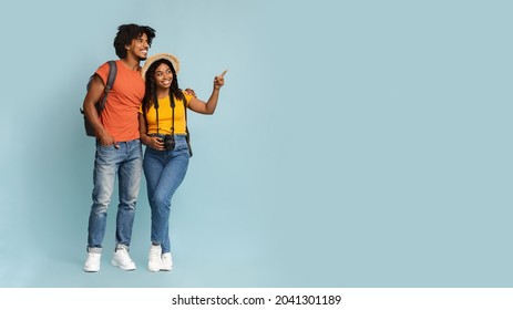 Happy millennial black couple tourists with backpacks and camera embracing and looking at copy space on blue studio background, choosing destination to travel, panorama. Travelling concept - Shutterstock ID 2041301189