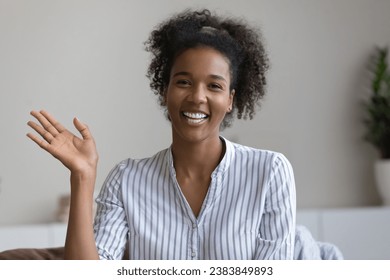 Happy millennial Black girl, young woman waving hello at webcam, smiling at camera, making video call from home, greeting and talking at online conference. Screen view, head shot portrait - Powered by Shutterstock