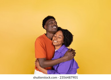 Happy millennial black guy hugging lady, enjoy love, isolated on yellow studio background, copy space. Romantic date together, free time, couple emotions, lifestyle, ad and offer - Powered by Shutterstock