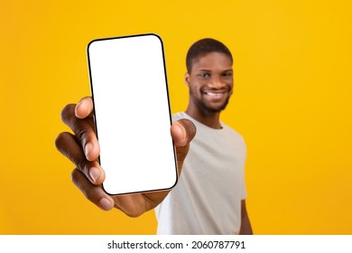 Happy millennial black man showing modern mobile phone with blank display for text or advertisement on yellow studio background, recommending newest mobile application, copy space - Shutterstock ID 2060787791