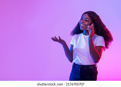 Happy Millennial Black Woman Talking On Smartphone In Neon Light, Free Space. Positive Young African American Female Making Phone Call, Smiling And Having Friendy Conversation