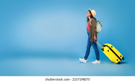 Happy Millennial Black Woman Walking With Suitcase, Traveling Abroad, Having Summer Vacation On Blue Studio Background, Copy Space. Young African American Lady Having Tour, Enjoying Voyage, Banner