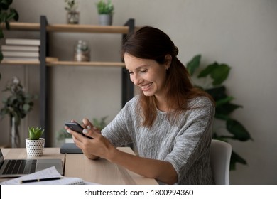 Happy millennial Caucasian female sit at desk at home have fun texting messaging on modern smartphone gadget, smiling young woman laugh watching funny video on cellphone, use technology on cell - Powered by Shutterstock