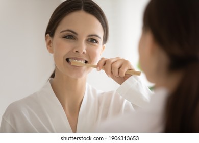 Happy millennial Caucasian woman hold eco wooden toothbrush clean teeth in home bathroom. Smiling young female use bamboo ecological brush for dental oral routine. Dentistry, fresh breath concept. - Powered by Shutterstock