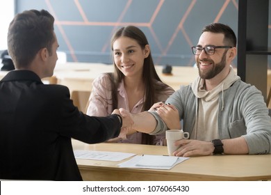 Happy millennial couple handshaking realtor making real estate deal, smiling clients and architect shaking hands, mortgage loan investment contract for new house purchase or construction concept