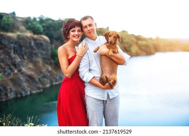 Happy Millennial Couple Hugging Standing Outdoors Holding Dachshund Dog, Childfree Spouses Enjoy Time Together Having Fun With Dog