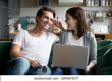 Happy Millennial Couple Laughing Joking With Laptop Together On Kitchen Sofa, Smiling Young Girl And Guy Having Fun Talking At Home On Couch Using Computer, Cheerful Family Enjoy Weekend With Device