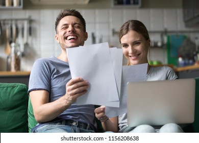 Happy millennial couple laughing reading good positive funny information in paper bills or letters, young smiling man and woman having fun with documents and laptop while planning budget finances