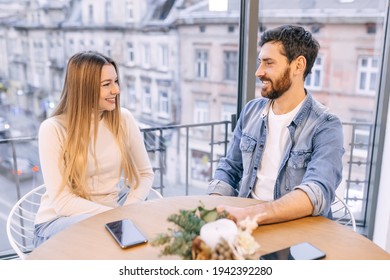 Happy Millennial Couple In Love Talking Sitting At Coffee House Table Together, Smiling Young Attractive Man And Woman Chatting And Flirting Enjoying Pleasant Conversation, Date.