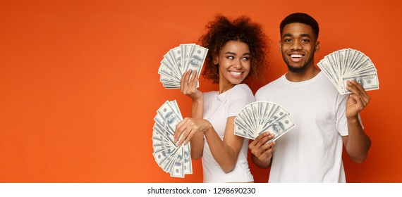 Happy Millennial Couple Posing With Lot Of Money, Holding With Dollar Fans, Orange Panorama Background With Empty Space