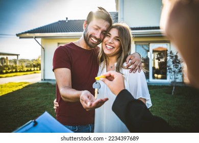 Happy millennial couple receiving keys from realtor, purchasing real estate - Family meeting with real estate agent - New house and real estate concept - Shutterstock ID 2234397689