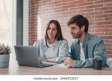 Happy millennial couple sit at table at home browsing web on laptop shopping online together, smiling young husband and wife work on computer at desk pay household bills or taxes in internet banking - Powered by Shutterstock