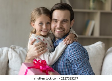 Happy Millennial Dad Embracing Beloved Daughter Kid With Love, Tenderness, Gratitude, Holding Pink Gift Wrap, Celebrating Fathers Day, Birthday, Looking At Camera, Smiling. Head Shot Portrait