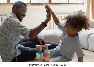 Happy Millennial Dad Giving High Five To Toddler Son, Celebrating Building Pyramid From Wooden Blocks. Happy Kid Playing Learning Games With Daddy On Heat Floor. Parent Teaching Child Concept