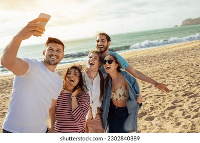 Happy millennial european and arabic friends have fun, taking selfie on smartphone, enjoy free time on ocean beach. App for blog and social network, outdoor party, holiday and trip - Powered by Shutterstock