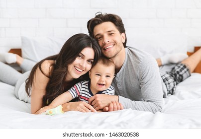 Happy millennial family bonding on bed, spending weekend morning together