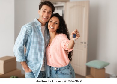 Happy millennial family holding and showing key standing in their new apartment flat. Cheerful guy and young lady moving to own house, unpacking belongings, selective focus on hand, free copy space - Shutterstock ID 2075626849