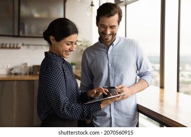 Happy millennial female employee showing online project presentation on digital tablet to skilled male team leader during coffee break pause time, discussing working issues in modern office kitchen. - Powered by Shutterstock