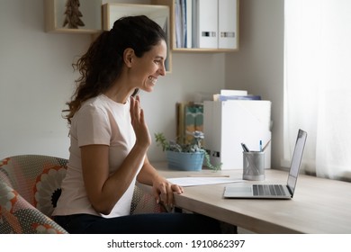 Happy millennial female sitting by laptop pc making video call using device webcam. Friendly young woman teacher tutor start distant lesson from home using conference app waving hand welcoming pupils - Shutterstock ID 1910862397