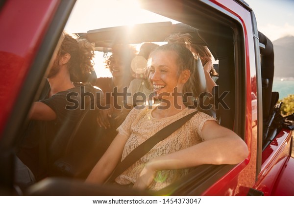 Happy millennial friends on a road\
trip vacation driving in an open car, close up, lens\
flare