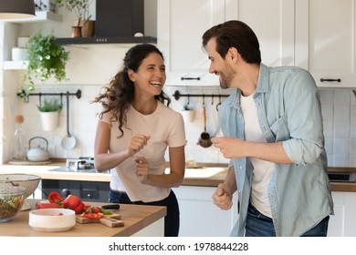 Happy Millennial Gen Married Family Couple Listening Energetic Disco Music, Dancing Together In Modern Kitchen. Distracted From Cooking Preparing Food Joyful Man And Woman Having Fun Entertaining.