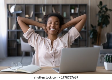 Happy millennial generation african ethnicity woman resting on chair with folded arms behind head and closed eyes, feeling relaxed on after finishing difficult online project on computer in office.