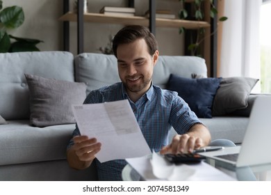 Happy Millennial Generation Man Managing Holding Paper Bills, Enjoying Doing Domestic Paperwork, Calculating Monthly Budget Or Expenses, Making Online Payments In E-banking App, Accounting Concept.