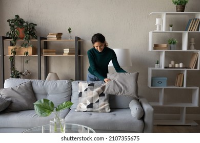 Happy millennial generation positive beautiful young housewife cleaning apartment, arranging stuff in cozy modern living room, put things on right places, feeling satisfied with comfort tidy house.