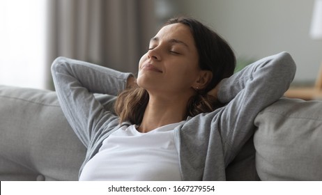 Happy millennial girl with eyes closed relax on comfortable couch in living room take nap daydream at home, smiling young Caucasian woman rest on cozy sofa breathing fresh air, stress free concept