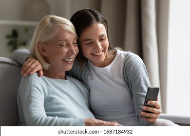 Happy Millennial Girl And Senior Mom Sit On Couch At Home Smile For Self-portrait Picture On Cellphone Together, Overjoyed Mature Mother And Adult Daughter Relax On Sofa Take Selfie On Smartphone